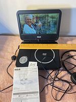 RCA portable DVD player powered on displaying an image, sitting open with control buttons visible and cables attached.