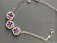 Close-up of silver bracelet with three purple amethyst gemstones in floral settings and adjustable chain clasp.
