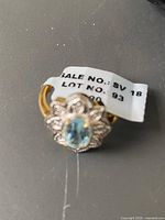 Close-up photo of the ring with a sale tag, showing the blue topaz center stone and white topaz accents with a gold colored band.