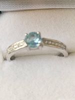 Close-up shot of the silver ring front showing light blue round topaz gemstone and engraved silver band.