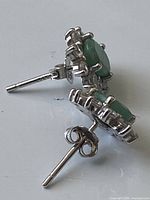 Close-up side view of the silver stud earrings showing the green emerald and silver prongs with butterfly back for securing.