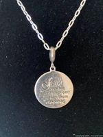 Front side of silver pendant with engraved inspirational faith text.