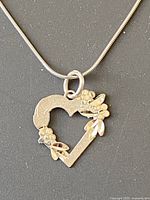 Front view of the silver heart-shaped pendant necklace with floral detailing on a flat dark surface, showing floral accents and chain loop.