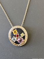 Front of silver circular pendant showing multiple gemstones of yellow, red, green, blue, and purple colors.