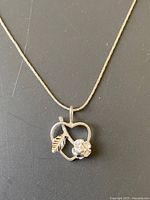 Close-up of the silver pendant shaped like an apple with a leaf and flower detail with stones.