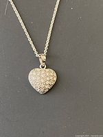 Close-up of the heart-shaped pendant on silver chain, showing detailed stone setting and chain links.