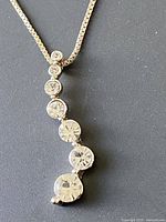 Close-up photo of the pendant showing seven clear round gemstones of increasing size set vertically on silver-tone bezels.