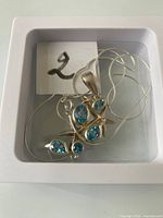 Top view of the necklace pendant with five blue topaz stones and starfish design, in white box.