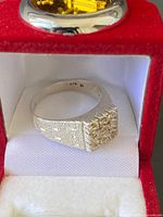 Silver ring inside red and white box showing 925 stamp inside the band and textured top with stones.