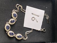 Silver bracelet with six blue sapphires on black cloth background, showing front design and chain clasp