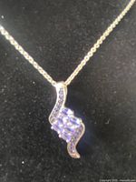 Close-up photo of the silver necklace pendant featuring a rectangular-cut central tanzanite gemstone and small clear stones accenting it, laid on black fabric.