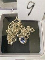 Silver necklace with blue topaz pendant tangled inside a protective box.