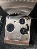 Rear view of the clock with three control dials for alarm and time settings, mounted on a stainless steel plate with engraved serial numbers.