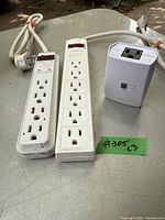 Photo showing two white power strips with multiple outlets and an APC UPS device