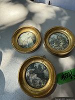 Top view of three round gilded frames with classical prints inside, showing aged boards and decorative edges.