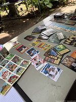 Photo showing various collectible cards including sports and game cards arranged on a table outdoors.