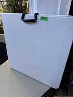 Image of the folding table closed, showing the white surface and black plastic handle for carrying.