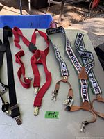 Four suspenders laid out on a green surface including black, red, and Heineken branded ones