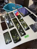 Photo of multiple used smartphones and a tablet displayed on a table, some with cracked screens.