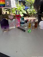 Photo showing the full set of various ladies perfume bottles on a table outdoors including two white empty bottles, a purple Hamlet Selection bottle, a square bottle with pink writing, and a pink Juicy Couture bottle with heart cap.