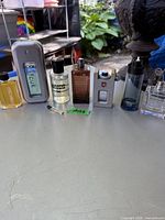 Full view of seven men's cologne bottles arranged in a row on an outdoor surface with plants in background.