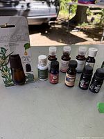 Photo showing a collection of 10 small bottles of essential and fragrance oils arranged in front of a vehicle, placed on a table in outdoor light.