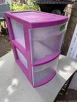 Front view showing two clear drawers with purple handles and purple top, unit on outdoor table.
