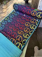 Full view of black quilted beach mat decorated with multicolor peace signs and attached bolster pillow at the top edge