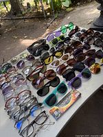 Wide view of sunglasses and eyeglasses on table showing various frames and lens colors including a boxed pair of Wiley X glasses.