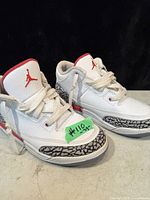 Front and side view of white kids Jordan running shoe with red details and elephant print accents, laced up.