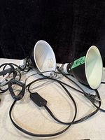 Pair of black clip-on lamps with clamps, showing power cords and inline switches on a light background with black backdrop.