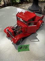 Red 1934 Ford pickup model with open hood showing detailed engine on table outdoors.