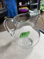 Clear glass vintage Kool Aid pitcher with handle and spout shown on outdoor table.