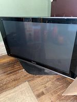 Front view of the 42 inch Panasonic plasma TV on a wooden floor, showing black bezel and screen.