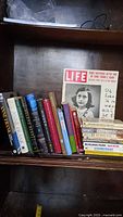 Bookshelf displaying 22 books about Anne Frank and related World War II history, with a LIFE magazine special edition prominently placed.