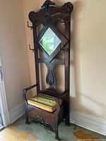 Full view of antique Victorian wooden hall tree with upholstered storage bench base, diamond-shaped mirror, and six metal coat hooks.
