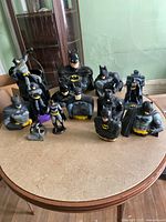 Full lot showing 13 Batman collectibles on round table, including bust banks, figurines and pail