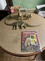 Full view of five metal dinosaur figurines on round table alongside Animals of the Past stamp book in plastic wrap