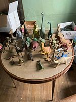 Multiple dinosaur figurines arranged on a round table, showing various dinosaurs in different colors and poses.