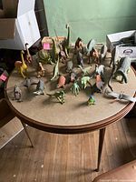 Overview of the lot showing about 27 dinosaur figurines in different sizes and colors arranged on a round table.