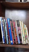 Wide shot of all 27 Elvis Presley books and magazines upright on a wooden shelf showing spines with varying titles and colors