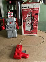 Robot toy with wired remote control and original packaging box on beige surface.