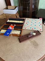 Overall view of both games showing Scrabble board, letter tiles in box, racks, and unopened Rummy box.