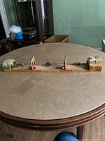 Full view of the elongated vintage tin wind-up toy with painted cityscape and mechanical features.