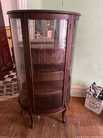 Front view of vintage wooden curio cabinet with curved glass panels and shelves inside