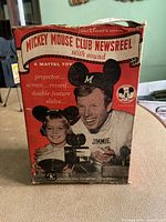 Front view of the Mickey Mouse Club Newsreel toy projector original box showing age wear and colorful branding with children and Mickey Mouse.