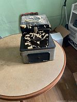 Front and top view of the Fleetwood record player unit with black grille and logo showing, along with the carrying case for the 45 RPM records featuring a black and white pattern including faces with sunglasses.