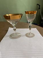 Two stemware glasses side by side on a table, showing gold rims and mid-century design