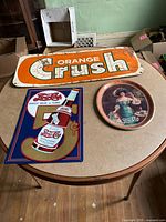 Overview of table showing all three items: Orange Crush sign, Pepsi-Cola sign, Pepsi serving tray
