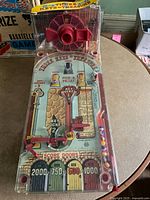 Full view of the vintage Three Keys to Treasure bagatelle pinball game on a round table, showing the colorful playing surface with key-themed scoring areas and flippers.